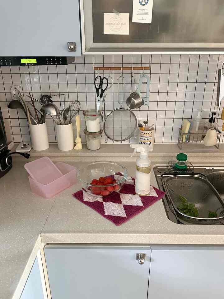 白いタイル壁とベージュのカウンターがあるキッチン、調理器具と洗剤ボトルが置かれた実用的な雰囲気のインテリア