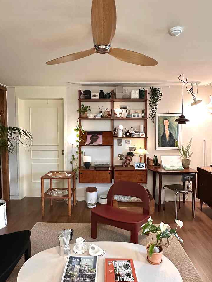 Wood tone and beige living room featuring a red armchair, shelves, floor lamp, and plants creating a warm atmosphere