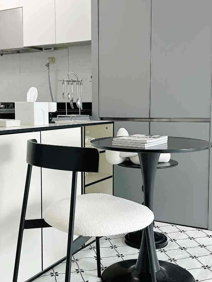グレーと黒のトーンのキッチンスペース、白いクッション付き黒いダイニングチェアと丸い黒いダイニングテーブルが配置されたモダンなおうちカフェインテリア