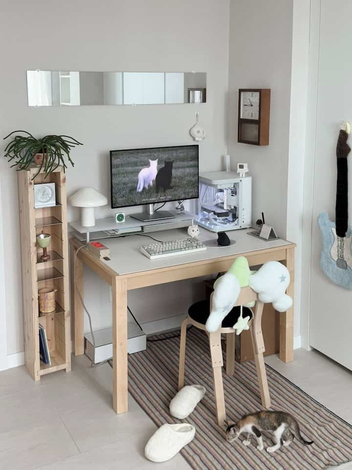 A cozy home office desk space featuring white and wood tones, with a monitor and a cat positioned on a patterned rug