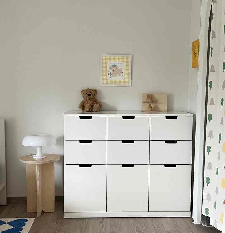 白と木目調が調和した子供部屋、中央に収納チェストが配置されたシンプルでナチュラルな雰囲気のインテリア