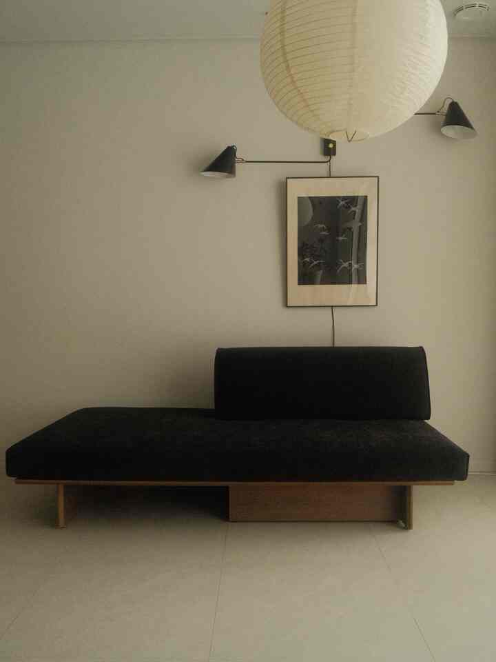 ナチュラルな木目調と黒のデイベッド、白い壁と照明が調和したミニマルなリビング空間