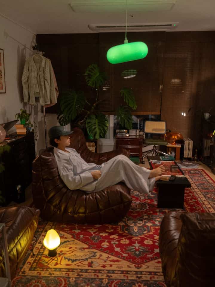 ダークブラウンのレザーソファと赤い柄のラグがあるリビング、緑のペンダントライトが雰囲気を演出する空間