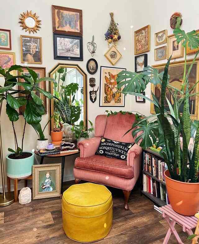 Natural-toned living room corner featuring pink armchair, yellow ottoman, abundant plants, and framed butterfly art with cozy atmosphere