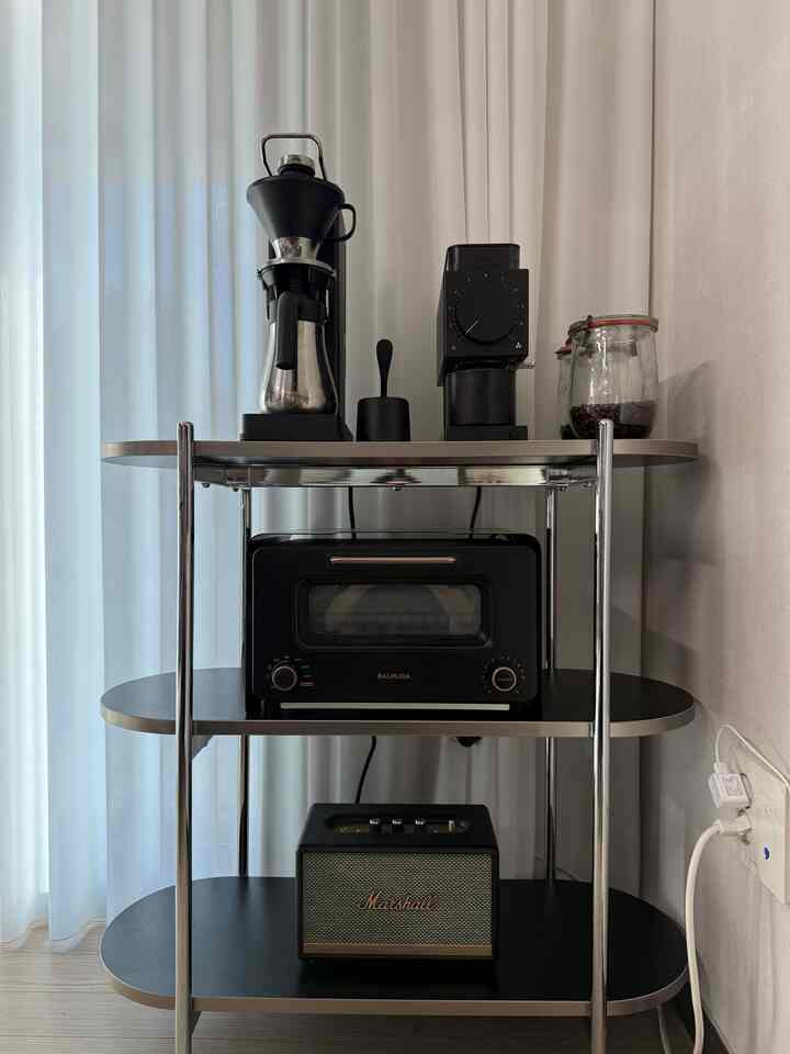 ブラックカラーの3段サイドテーブルにコーヒー器具とオーブンが配置されたコンパクトなキッチンスペース