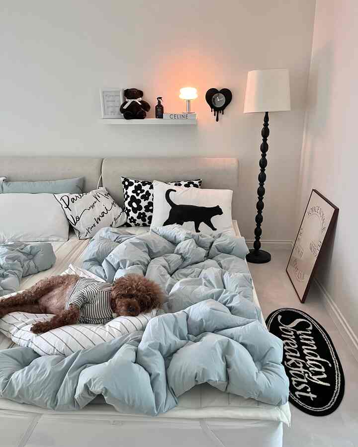 明るいベージュとパステルブルーの寝室、中央に犬が寝ているベッド、壁の棚とフロアランプ、ポスターが配置された雰囲気のあるインテリア