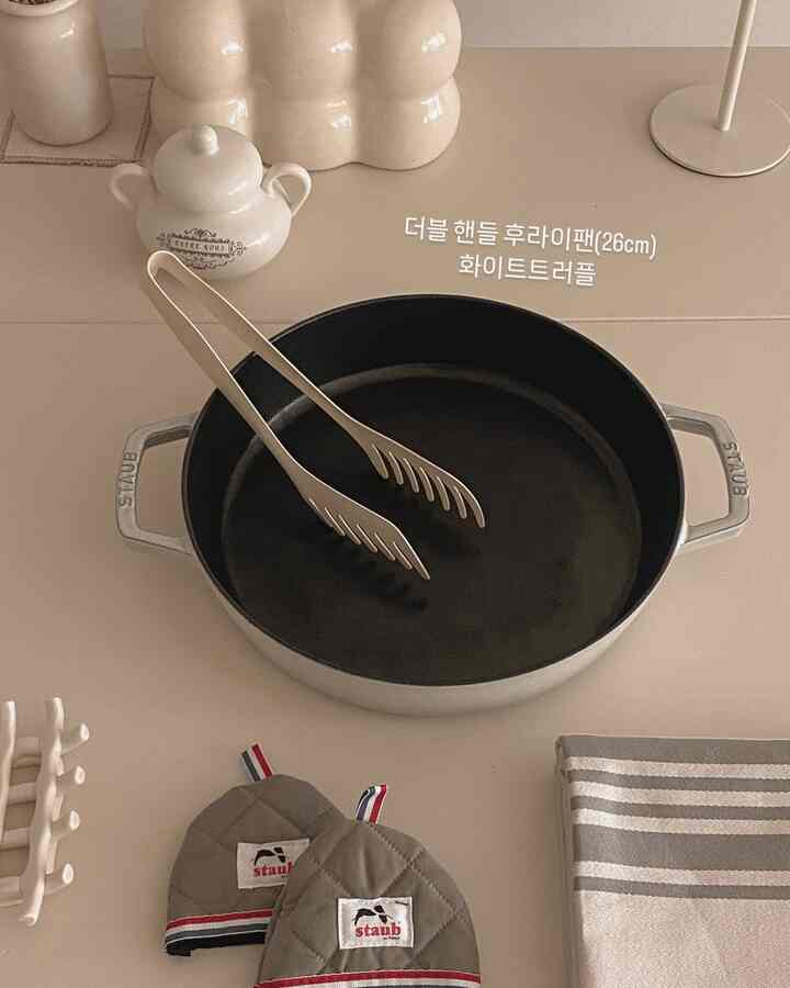 ナチュラルカラーとホワイトトーンのキッチン、ダブルハンドルのフライパンと整然とした調理器具が配置された印象的な空間