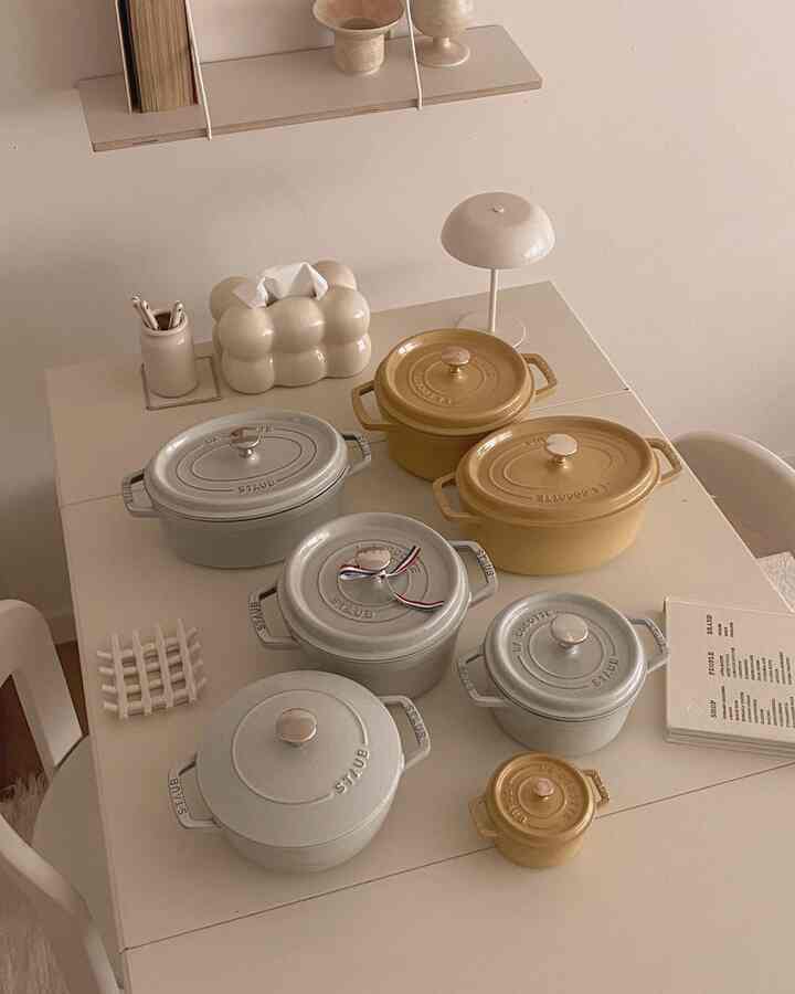 ベージュとホワイトのトーンのキッチンテーブルにスターウブのさまざまなサイズの鍋が整然と配置されたミニマルな空間