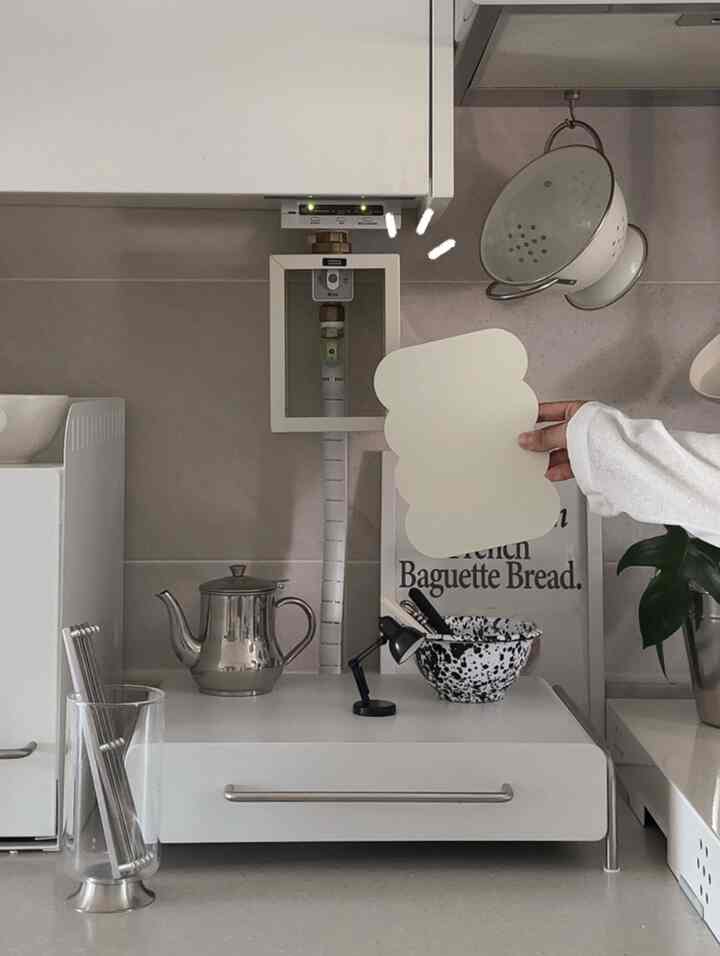 白とシルバー調のキッチン、ステンレス製ティーポットとテーブルランプが配置された清潔感のある空間