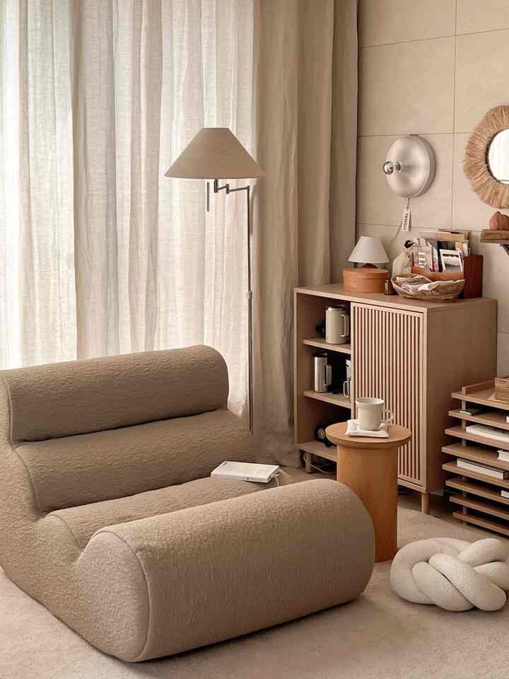 ベージュとナチュラルトーンのリビング、柔らかな曲線のソファと木製収納キャビネット、薄いリネンカーテンが調和した温かみのある空間