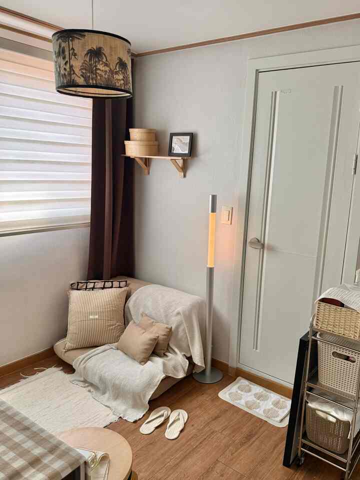 ベージュトーンと自然素材が調和した小さなリビング、シンプルなソファベッドとフロアランプが置かれた雰囲気のあるインテリア