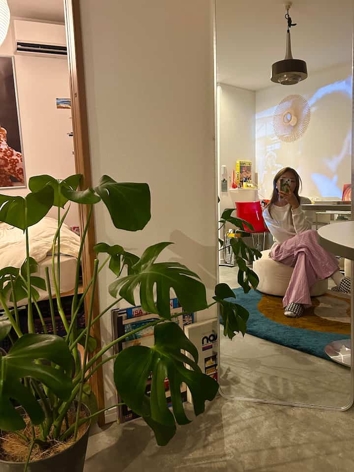 ナチュラルトーンの1LDK一人暮らし空間、全身ミラーとベージュのビーズクッション、多彩なラグと植物が配置されたミッドセンチュリーモダンのインテリア