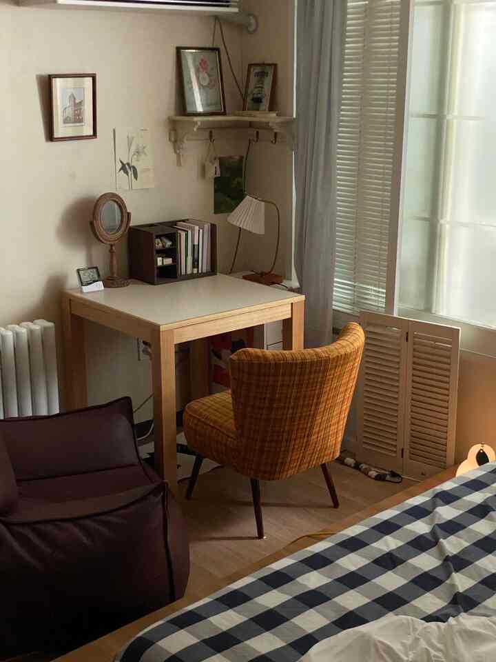 ベージュと木目調の調和がある寝室、木製デスクとビーンバッグソファ、チェック柄のアームチェアが配置された落ち着いた空間