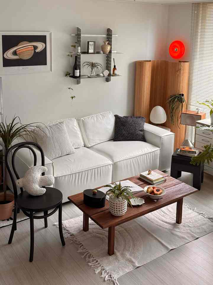 ホワイトとナチュラルの色調のリビング、清潔感のあるレザーソファと木製のコーヒーテーブル、植物と棚が調和した雰囲気のあるインテリア