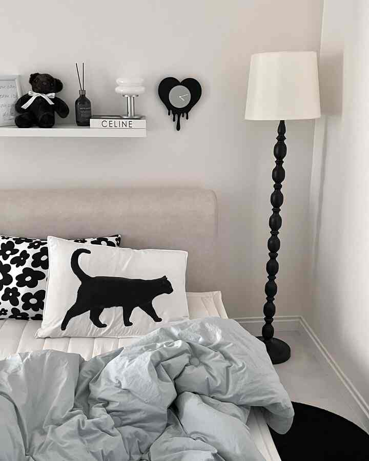 白と黒のトーンのシンプルモダンな寝室、猫柄クッションとフロアランプが配置された印象的な空間