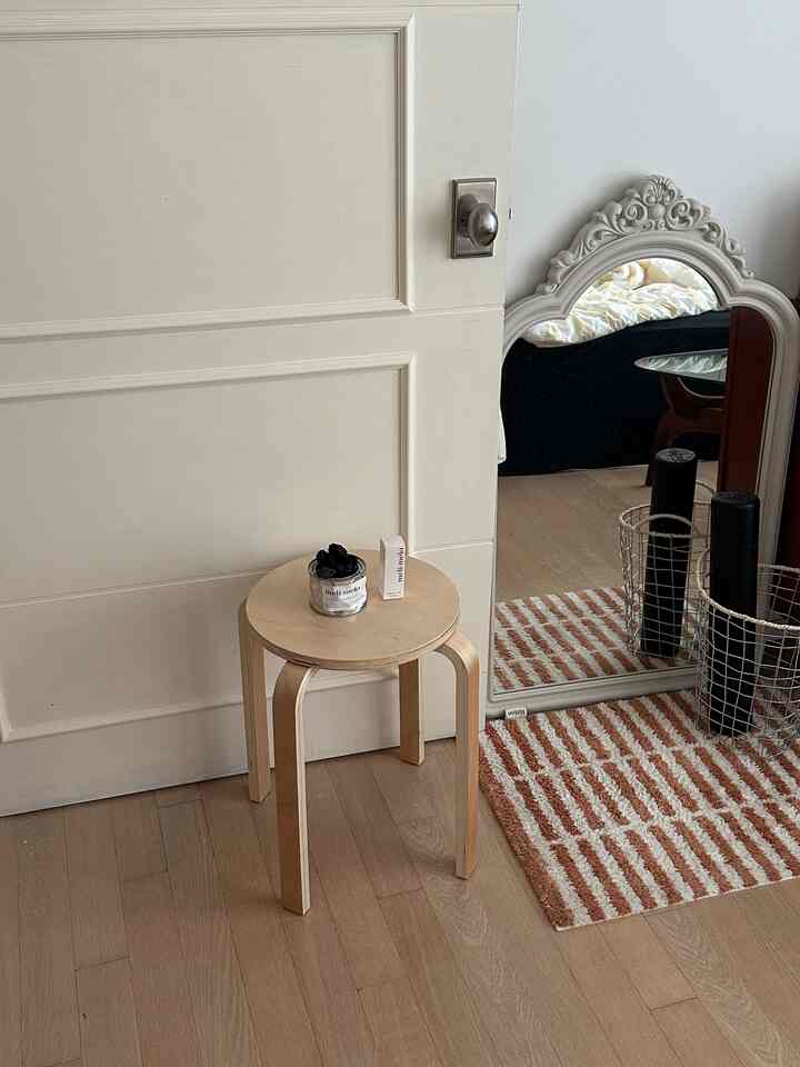 ナチュラルカラーの小さな玄関スペース、木製のスツールとクラシックな白い鏡が配置された落ち着いた雰囲気のインテリア