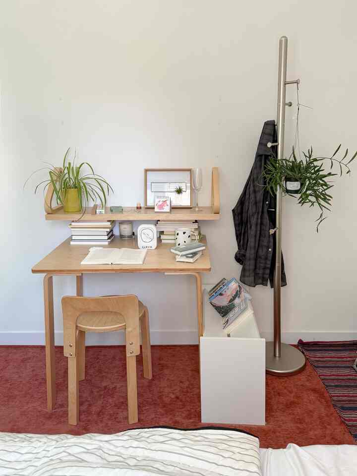 ナチュラルウッド調の寝室、木製デスクとチェア、スタンドハンガー、植物が配置された清潔で居心地の良い空間