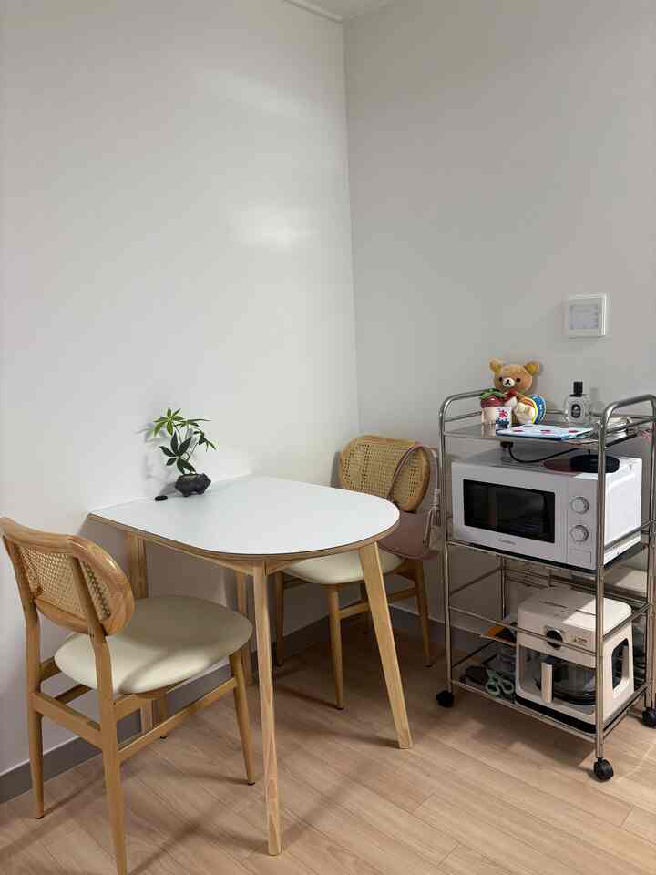 白い壁と木目調の家具が調和する二人用のダイニングスペースと、隙間収納のステンレス製トロリーが配置されたキッチンコーナー。