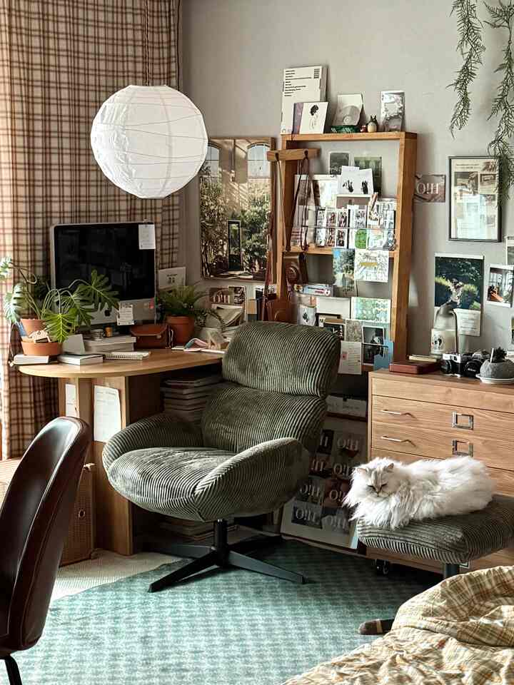 ナチュラルな木目調とグリーンのアクセントが調和するホームオフィス兼趣味スペース、居心地の良いアームチェアとふわふわのペットがいる温かみのあるワークスペース