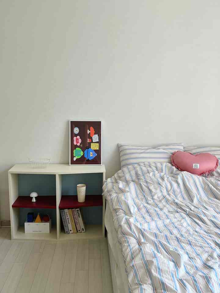 White walls and floor in a small studio bedroom featuring striped bedding and pink pillows, simple and minimal atmosphere