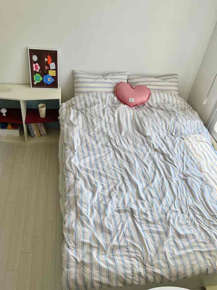 Simple bedroom with white and blue striped bedding, featuring a pink heart cushion as an accent