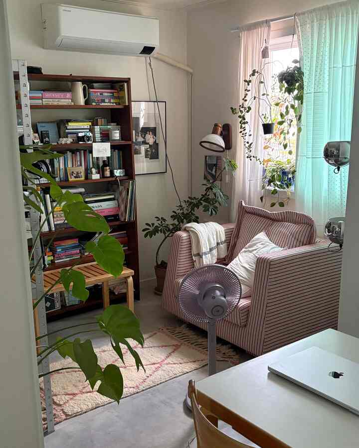 A small living room dominated by white walls and ceiling with a red-striped armchair and wooden bookshelf, featuring a natural and vintage ambiance