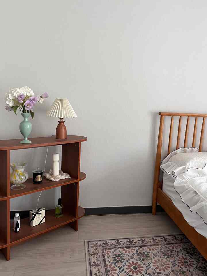 Natural bedroom with bright white walls featuring a mint vase, wooden bed frame, and shelf creating a calm atmosphere