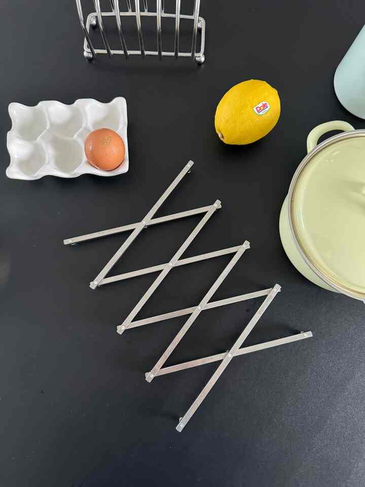 黒いキッチンカウンターに黄色のホーロー鍋、レモン、卵、ステンレス製鍋敷きが置かれたシンプルなキッチンのインテリア