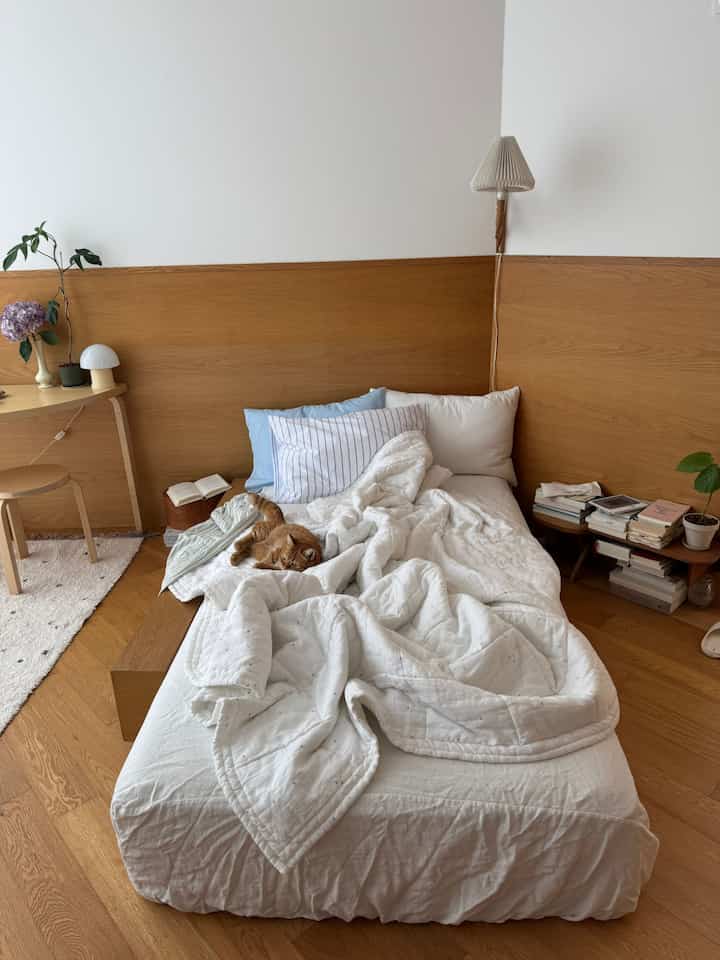 白と木目調が調和した寝室、居心地の良いベッドとデスクが配置され、猫がくつろぐ雰囲気のあるインテリア