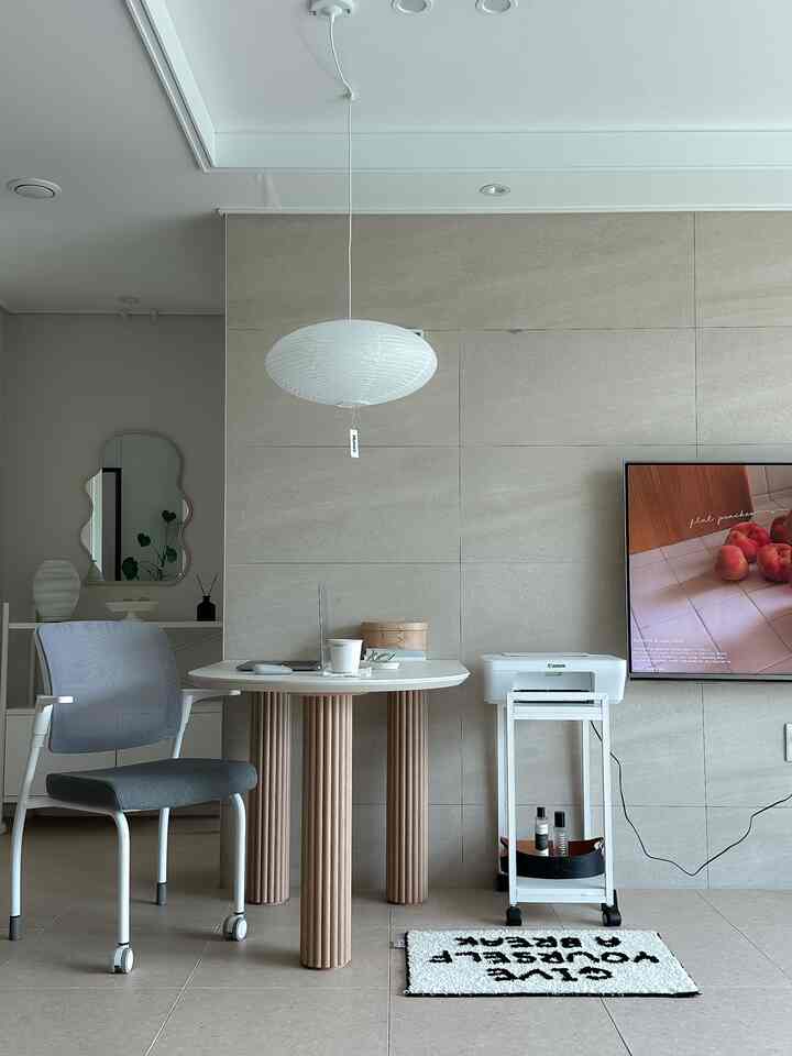 白とベージュのトーンのワンルームリビング、丸テーブル、オフィスチェア、プリンターが配置されたすっきりとしたホームオフィスのあるインテリア