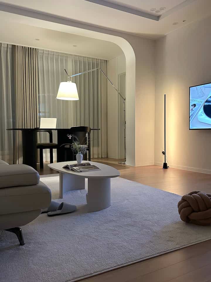 白とナチュラルモダン調のリビング、広いラグの上にソファとコーヒーテーブルが配置された印象的な空間