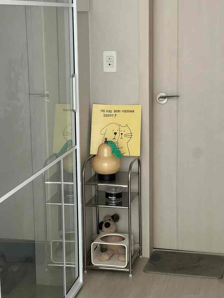 ベージュのトーンの小さなコーナー収納に犬のぬいぐるみとポータブルランプが配置された整った玄関スペース