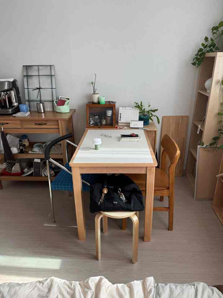 白い壁とナチュラルウッドの家具が配置されたコンパクトな空間、テーブルクロスのかかったダイニングテーブルと椅子があり、温かみのある印象的なインテリア