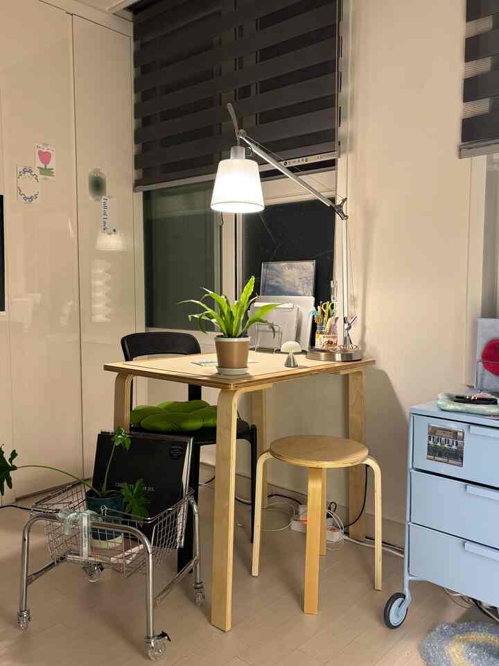 明るい木目調とホワイト・ベージュのトーンが特徴の一人暮らし用ホームオフィス、植物やスツール、照明が調和したミニマルなインテリア