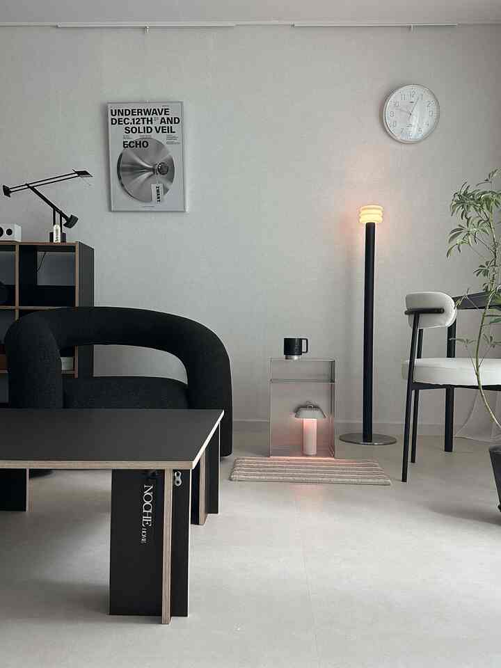 A monotone minimalist living room featuring a black stool, floor lamp, and transparent tables in a clean interior
