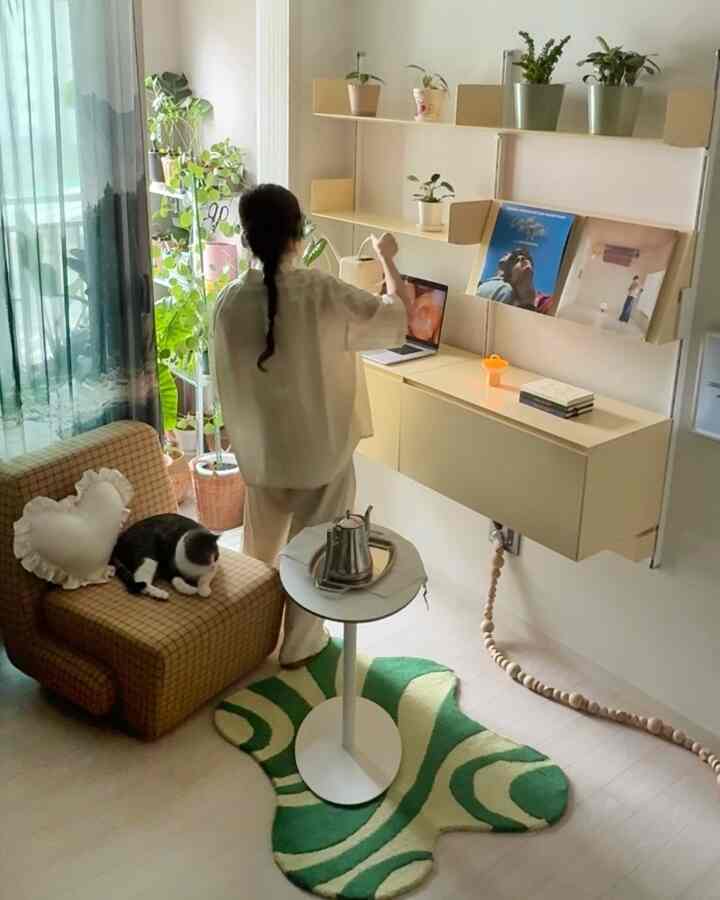 薄いベージュ色の壁とナチュラルトーンの家具が配置されたホームオフィス空間、植物と猫がいる印象的なインテリア
