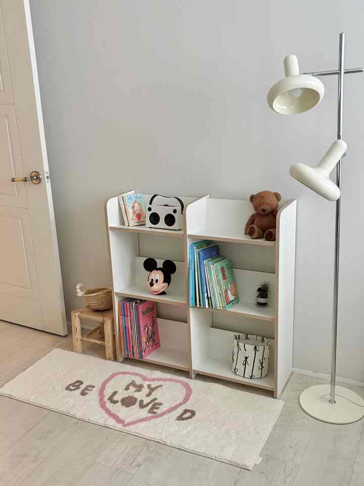 A white and wood-toned kids' room featuring a bookshelf and rug with a clean, cozy atmosphere