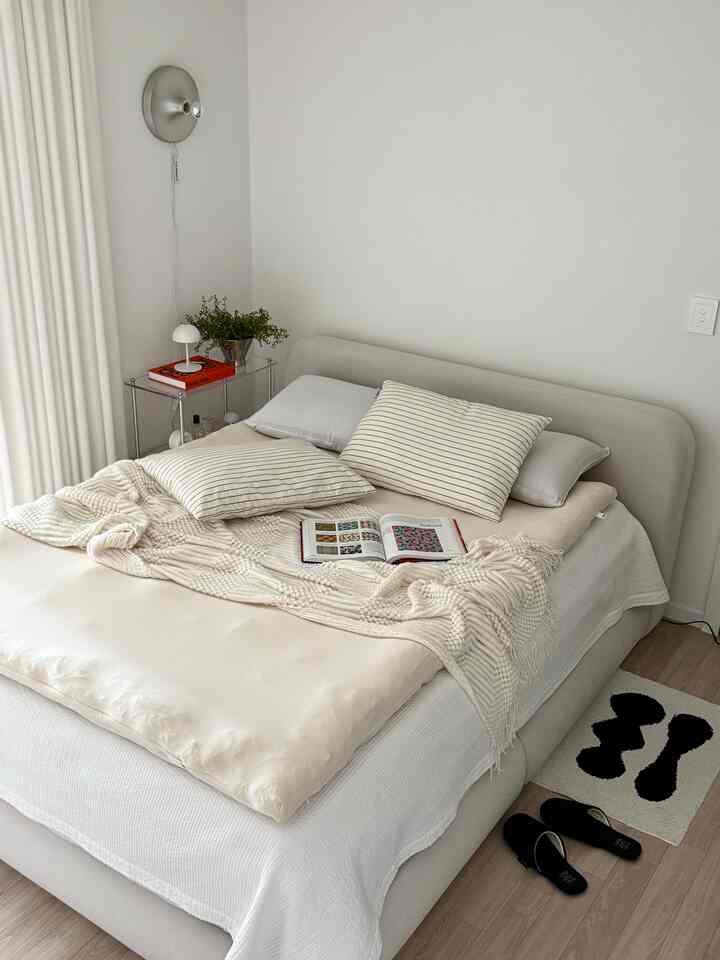 アイボリーの色調の寝室、ゆったりとしたベッドにブランケットが配置されたシンプルで心地よい空間