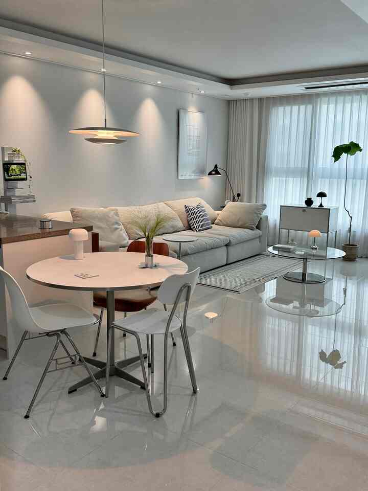 明るいホワイトトーンのモダンなリビングルーム、円形のダイニングテーブルとベージュのソファが配置された雰囲気のある空間