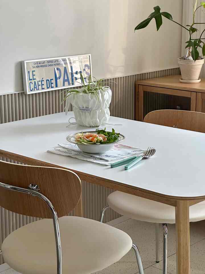 白と茶色のトーンのダイニングルーム、テーブルと椅子、観葉植物、額縁が配置された自然なモダンな雰囲気のインテリア