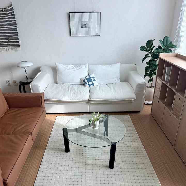 明るいホワイトとブラウンのトーンでまとめられたリビング、中央にホワイトのソファとガラスの円形コーヒーテーブル、自然光が入り込む落ち着いた空間