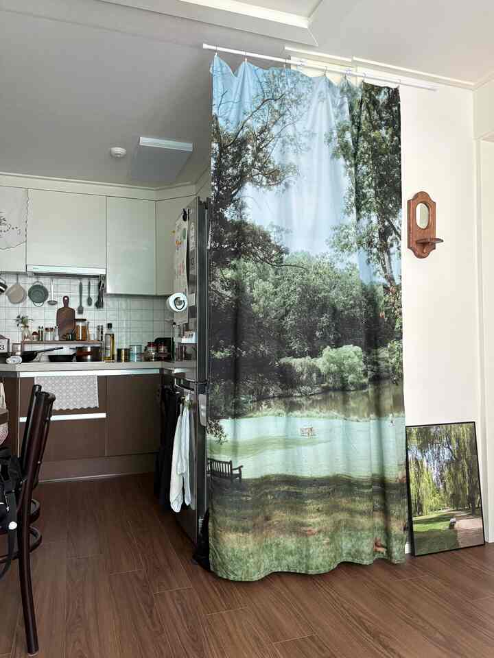 自然の風景がプリントされたカーテンがあるワンルームのキッチン、木目調の床と調和した居心地の良い空間