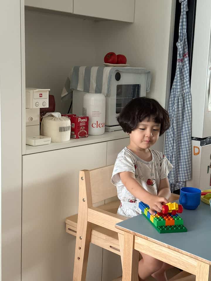 白と木目調のキッチンスペース、椅子に座った子供が玩具で遊んでいる、温かみのあるミニマルな雰囲気のインテリア