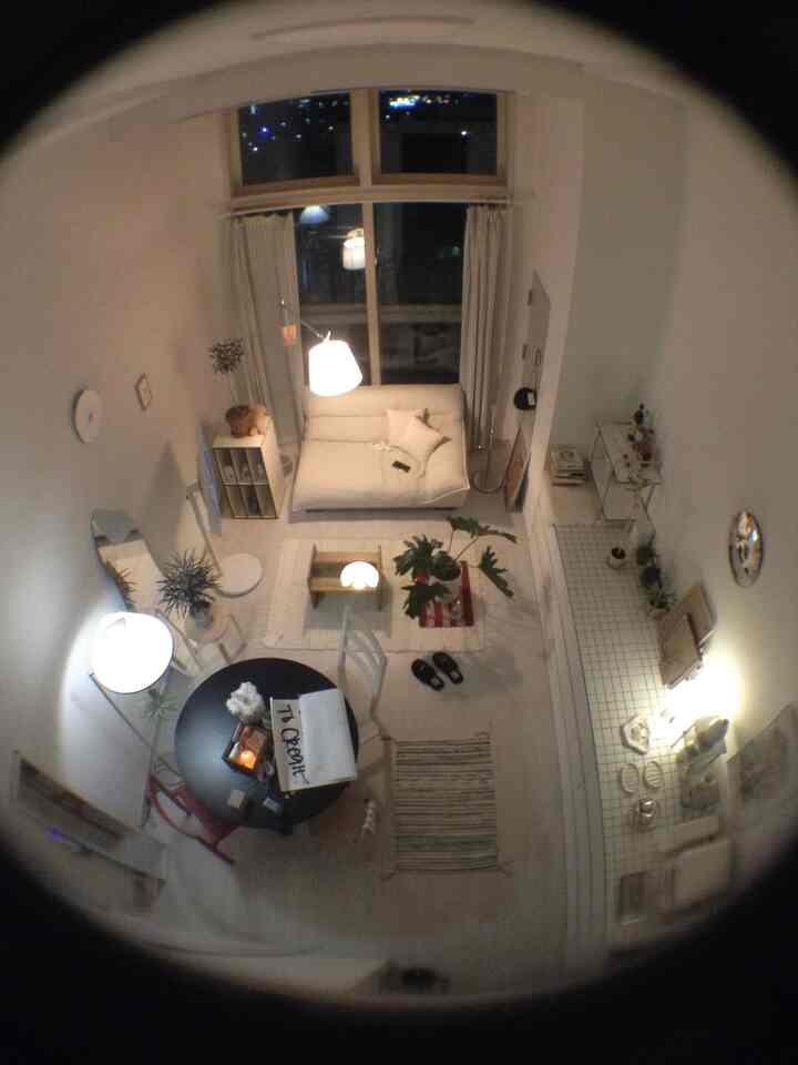 ホワイトと木目調を基調とした小さなリビング、シンプルなダイニングテーブルとソファ、フロアランプが配置されたミニマルなインテリア空間