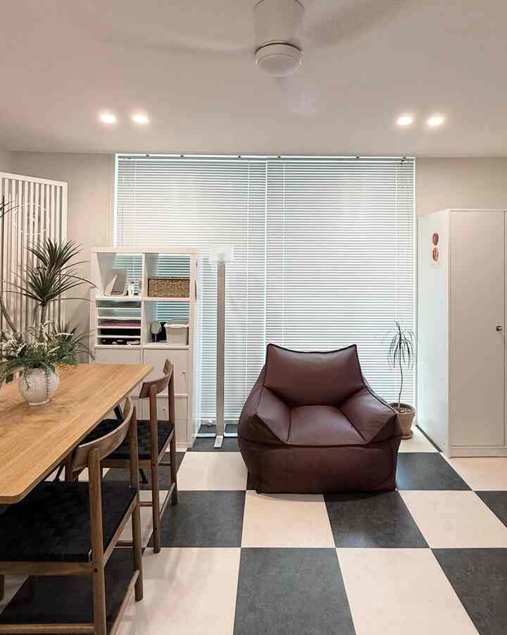 Modern living room in white and brown tones featuring a central brown bean bag and wooden dining table with chairs on the left