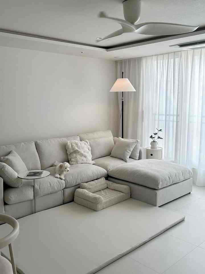 白を基調としたリビング、広いコーナーソファとペットベッドにいる小型犬、自然でシンプルな雰囲気のインテリア