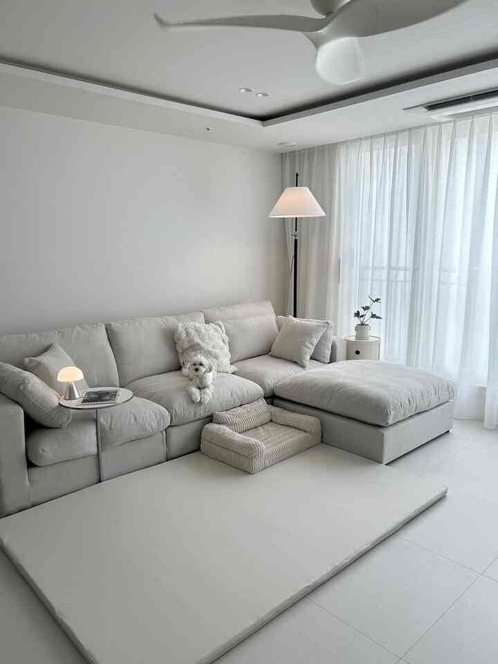 明るいモノトーンのリビング、モジュラーソファと赤ちゃん用マット、犬とラグが調和したモダンな空間