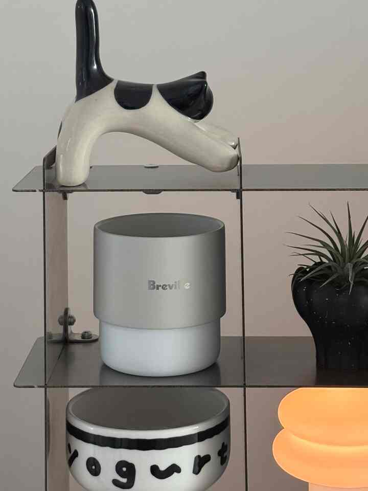 グレーと黒を基調とした棚に猫のオブジェ、Brevilleの容器、ヨーグルトボウル、小さな植物が配置されたミニマルなインテリアオブジェ