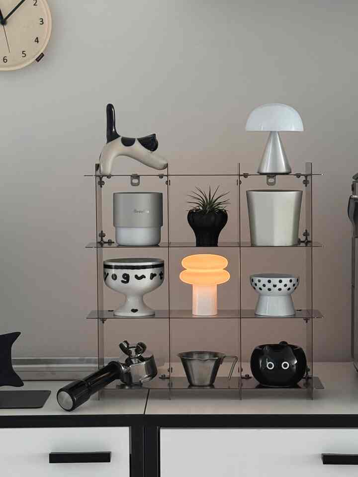 Calm white-toned kitchen space featuring transparent shelves with coffee tools and a small plant in minimalist style