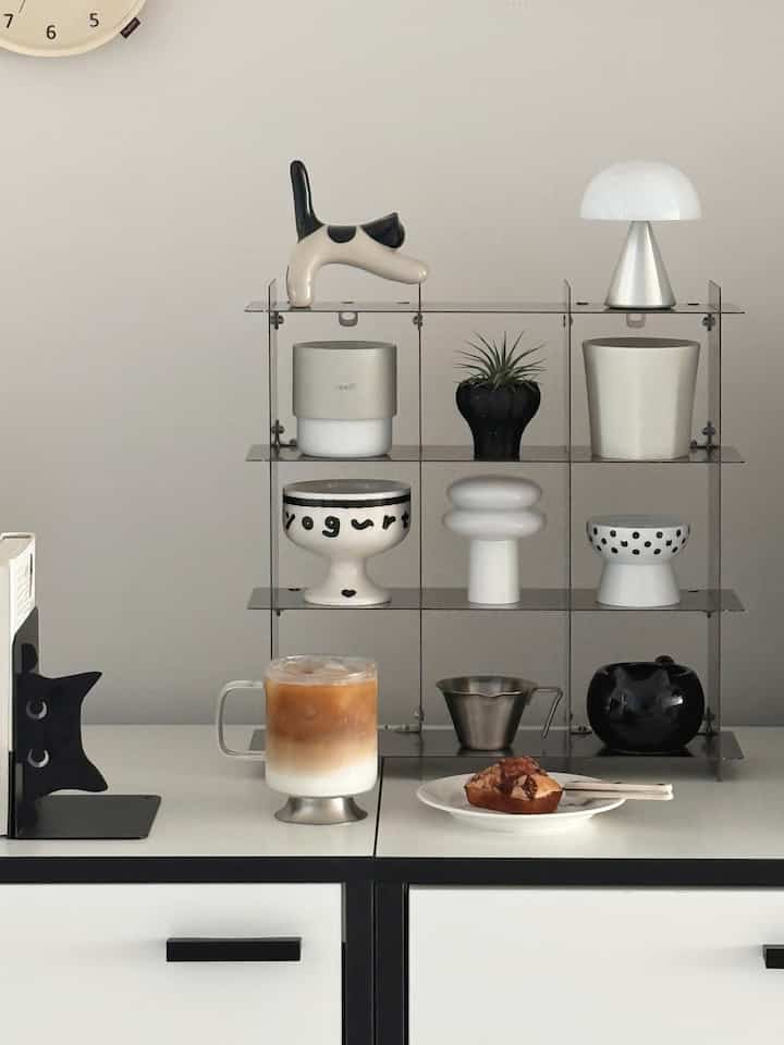 A clean modern kitchen counter in white and black features a metal shelf with assorted objets and a home cafe drink with snack.